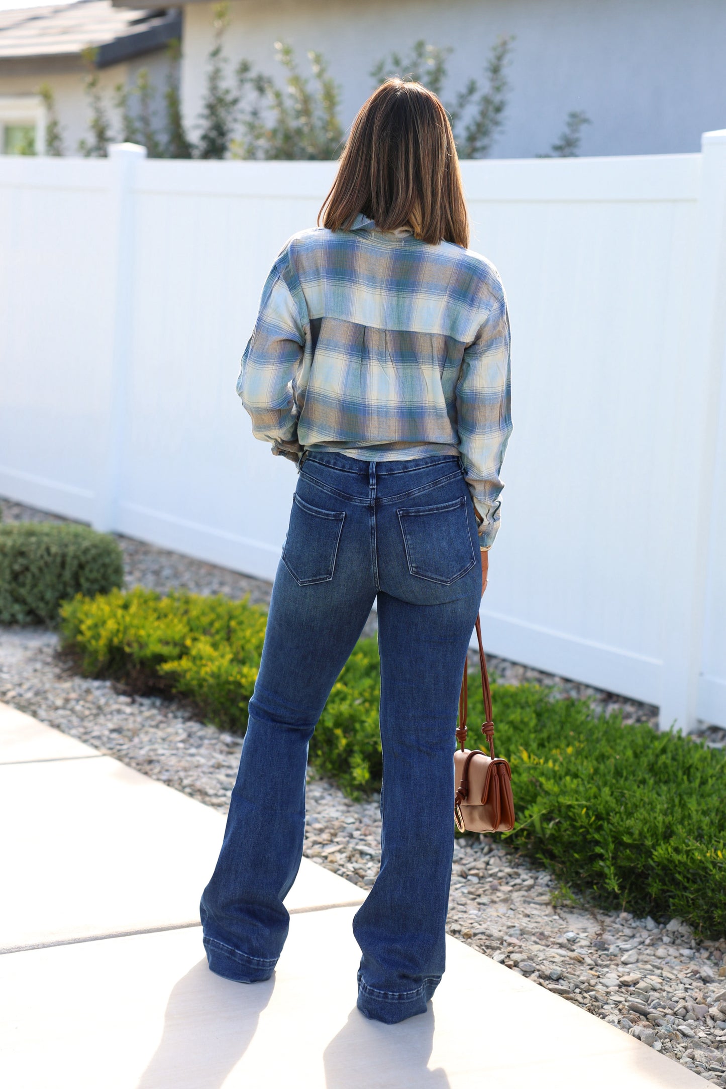 Outdoors, a woman in a plaid shirt and vintage style wears Medium Wash Flare Denim Jeans, holding a brown purse.