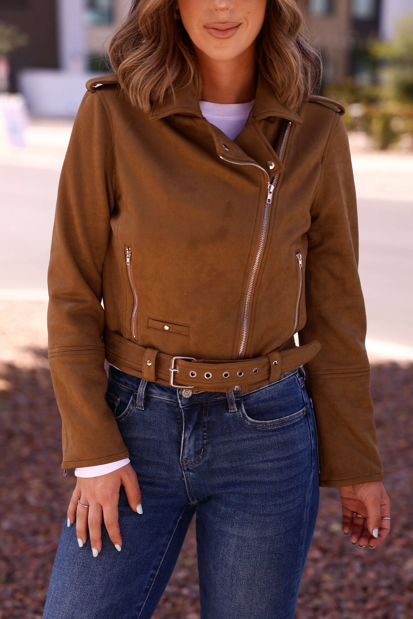 A woman outdoors wears the Audrey Taupe Vegan Suede Moto Jacket over a white top and blue jeans.