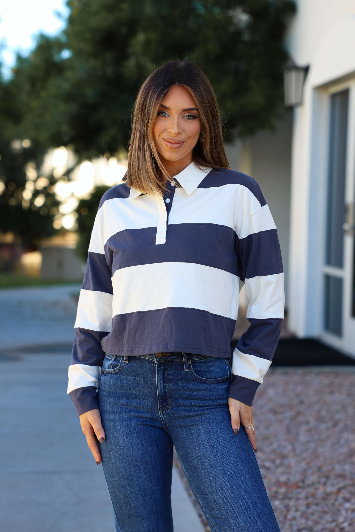 Woman smiling outdoors in a Thread and Supply Navy Stripe Button Up Top with a collared V neckline and jeans.