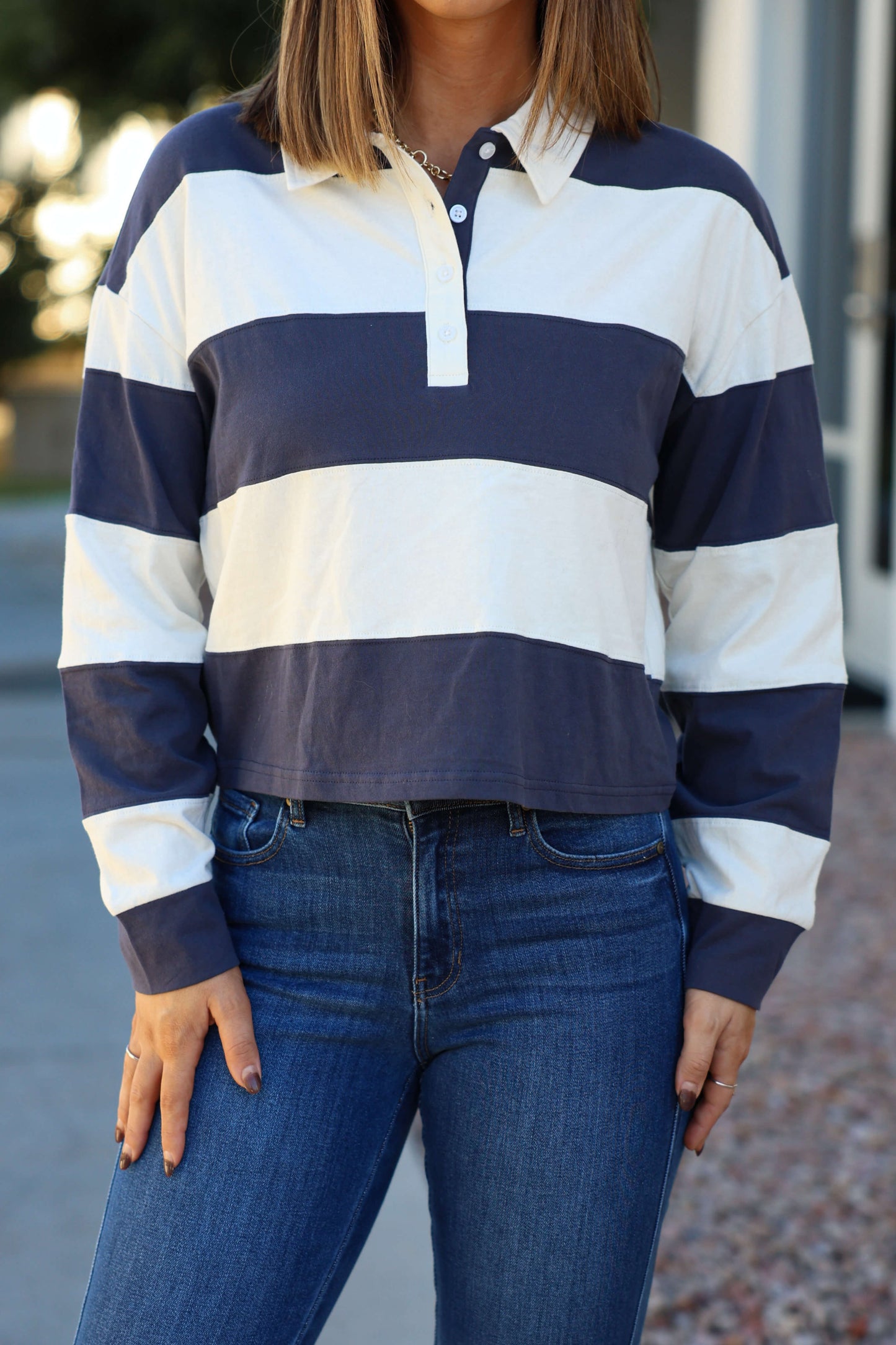 A person wearing the Thread and Supply Navy Stripe Button Up Top and blue jeans, standing outdoors.