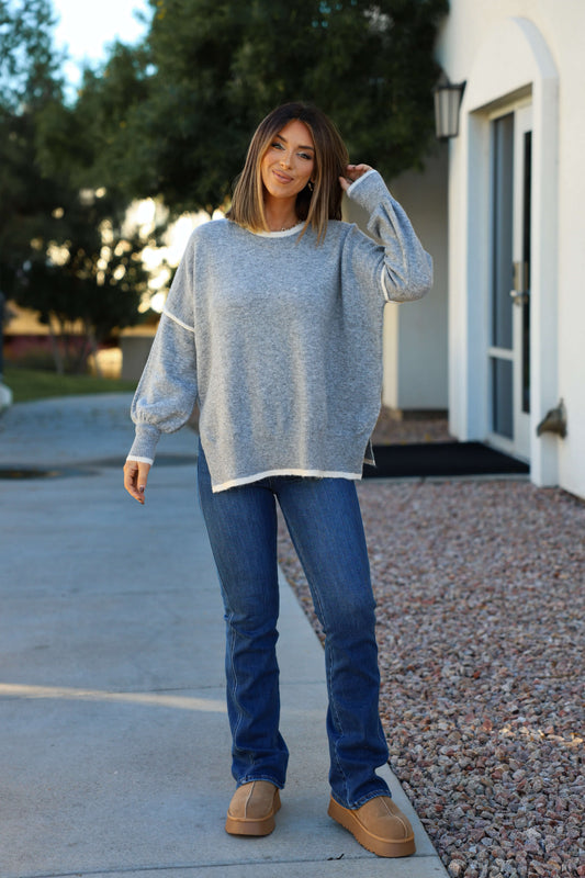Smiling woman outdoors in Grey Contrast Detail Pullover Sweater - FINAL SALE, blue jeans, and tan shoes touches her hair.