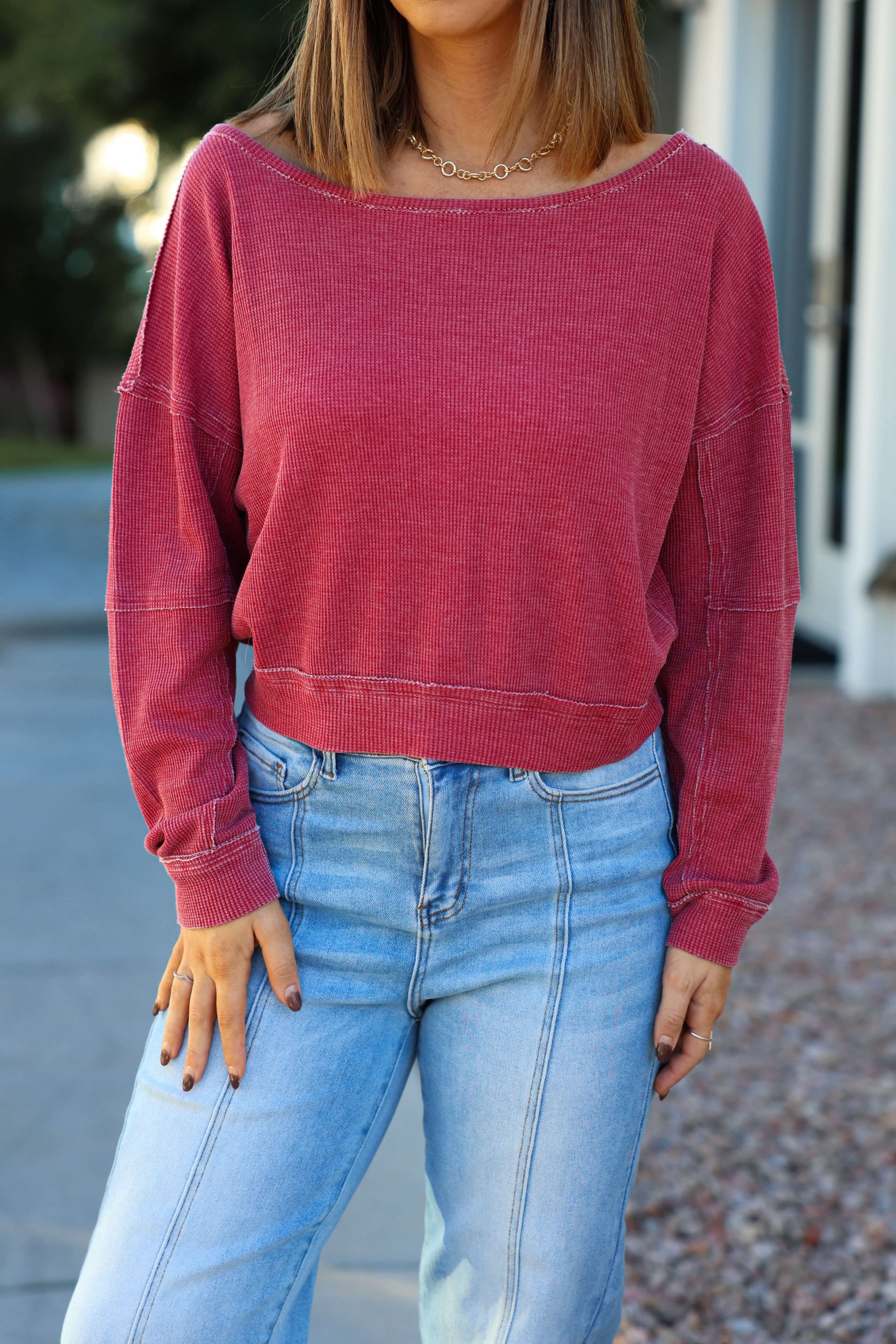 Woman wearing a Red Waffle Knit Boatneck Pullover and light blue high-waisted jeans, standing outside with a blurred background.