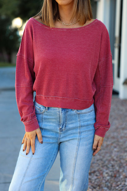 Woman wearing a Red Waffle Knit Boatneck Pullover and light blue high-waisted jeans, standing outside with a blurred background.
