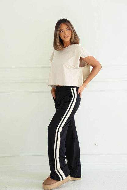 Woman indoors, smiling in beige top and Sporty Black Side Stripe Pants, paired with beige shoes.