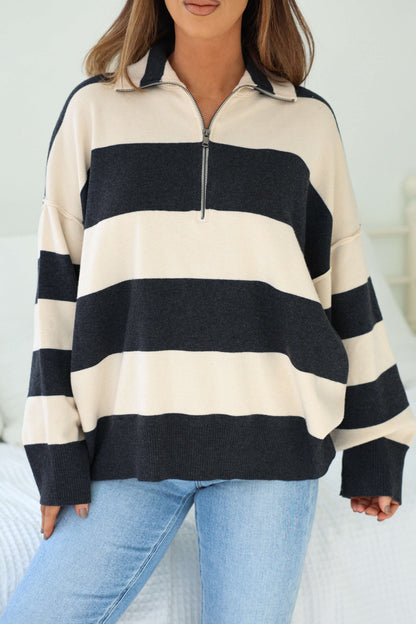 A woman indoors wears an Ivory and Charcoal Varsity Stripe Half Zip Rugby Pullover with light blue jeans.