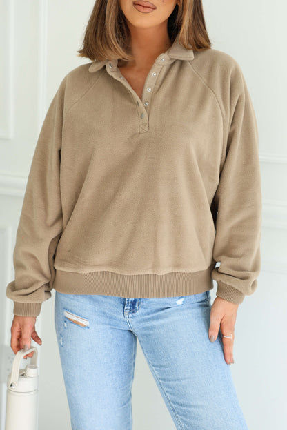 Woman in a Mocha Button Up Fleece Pullover and light blue ripped jeans holds a white water bottle, radiating cozy comfort indoors.