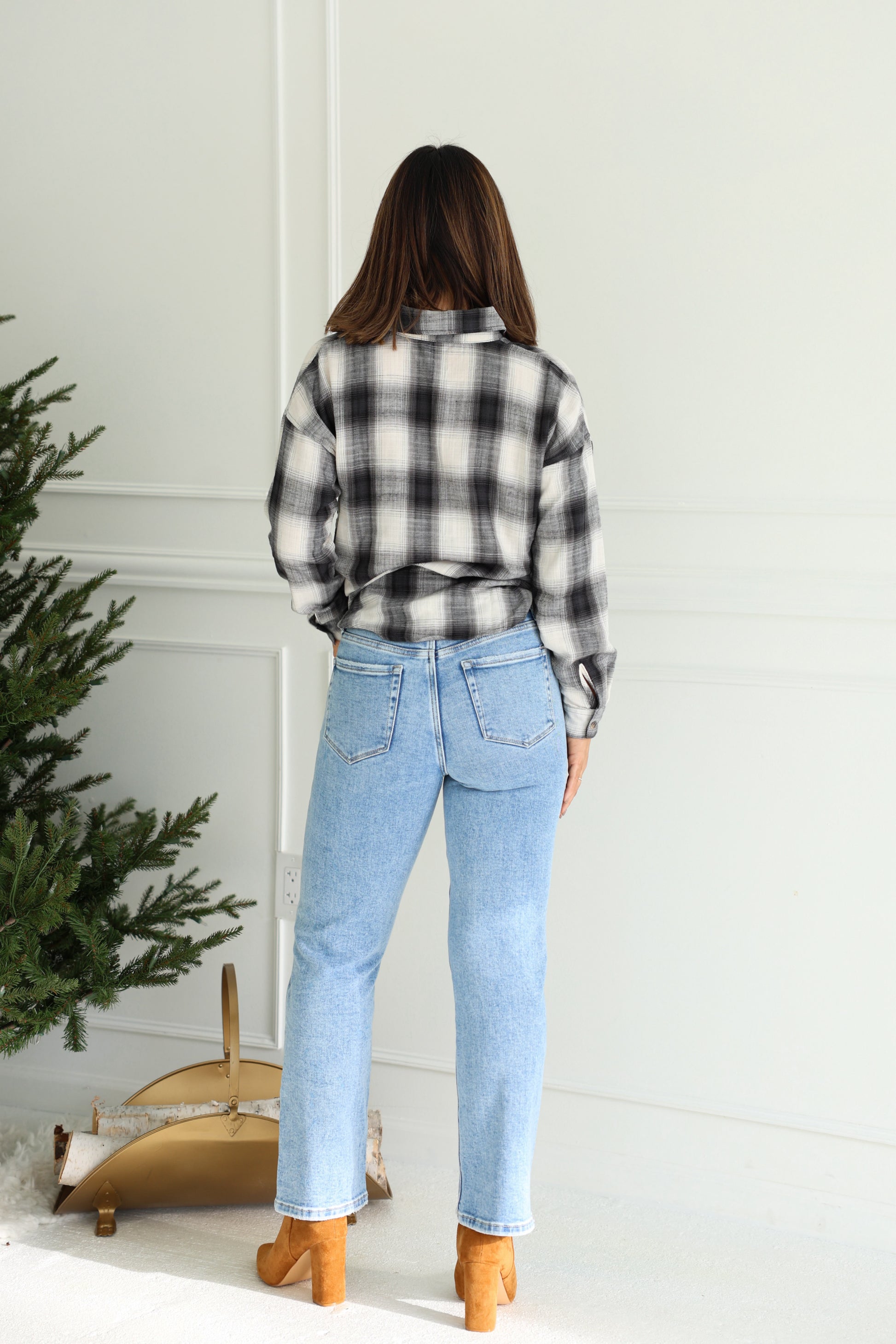 Woman stands by a small tree in a plaid shirt, Vervet Light Wash High Rise Cropped Jeans, and tan boots.