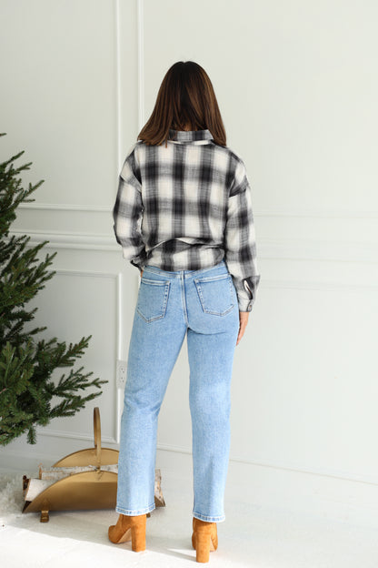 Woman stands by a small tree in a plaid shirt, Vervet Light Wash High Rise Cropped Jeans, and tan boots.