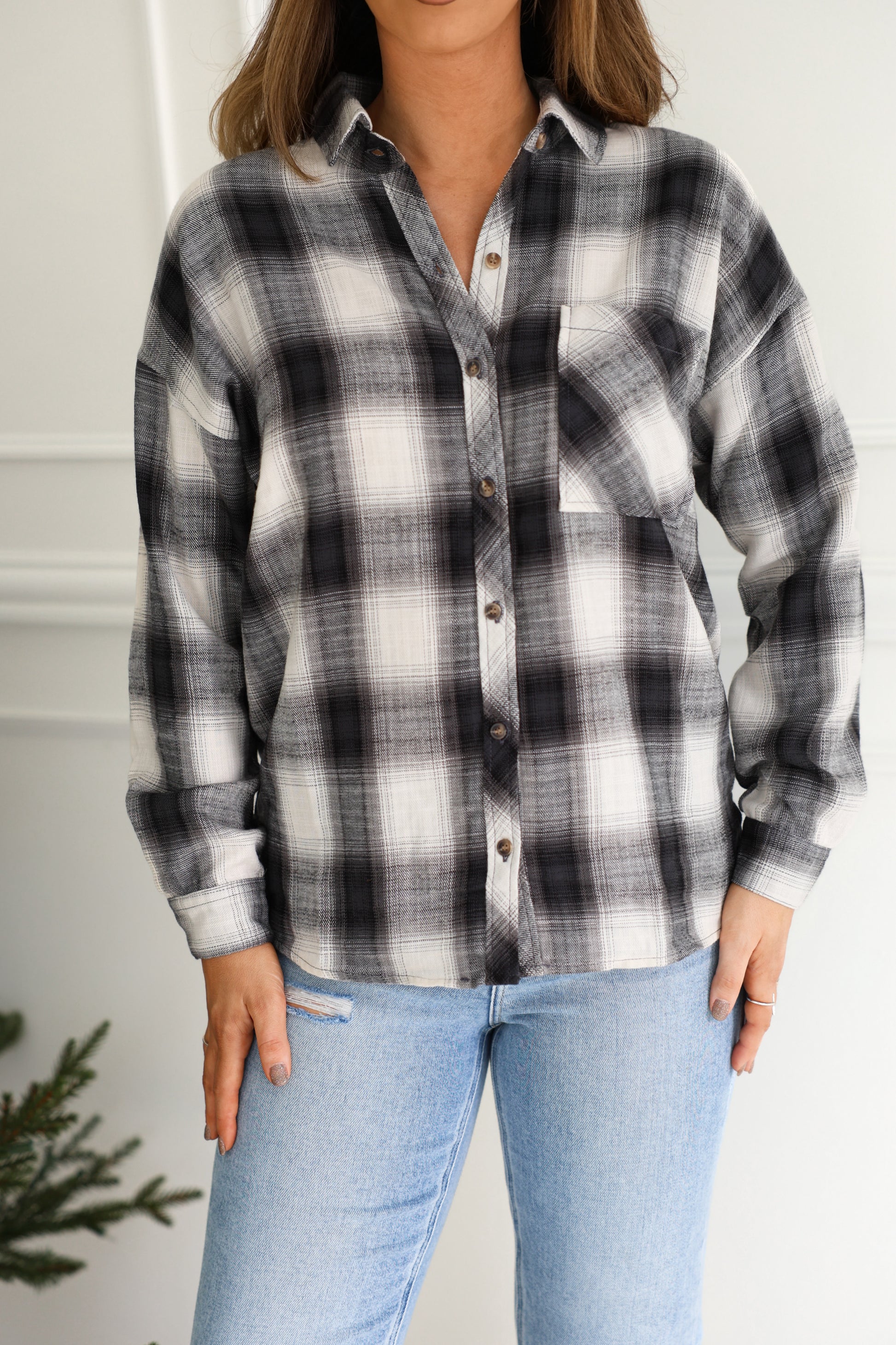 Someone layers the Madelyn Charcoal Plaid Flannel Shirt over light blue jeans for a relaxed indoor look.
