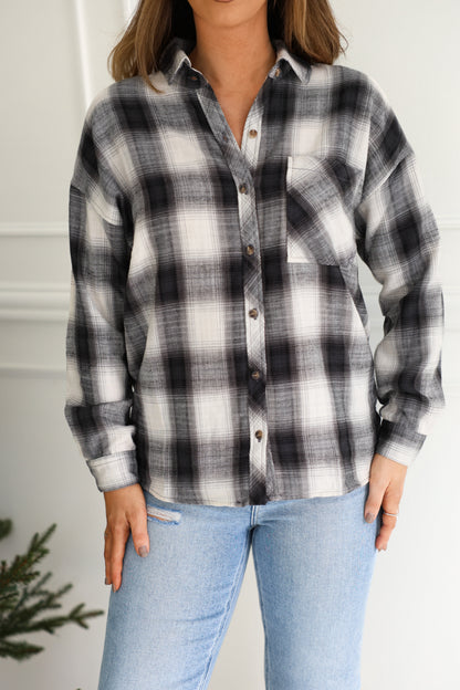 Someone layers the Madelyn Charcoal Plaid Flannel Shirt over light blue jeans for a relaxed indoor look.