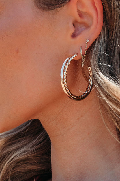 Close-up of a woman's ear wearing Dazzle Braided Hoop Earrings - Gold, layered with hoops and linked by a delicate chain to a stud.