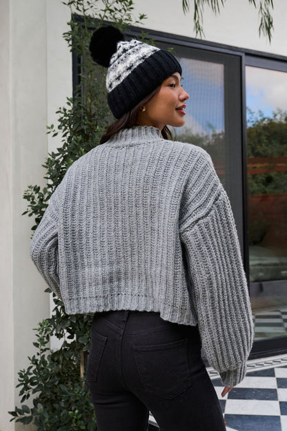 A woman in a Grey Wide Sleeve Ribbed Mock Neck Sweater, black jeans, and a beanie stands outside facing away.
