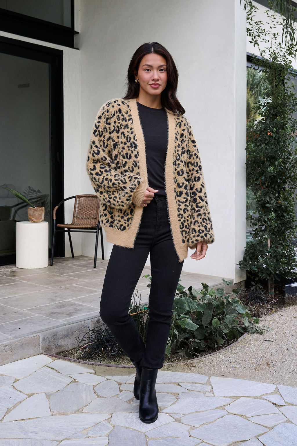 Woman outdoors in front of a house, wearing a Fuzzy Tan Leopard Open Front Cardigan, black top, black pants, and black boots.