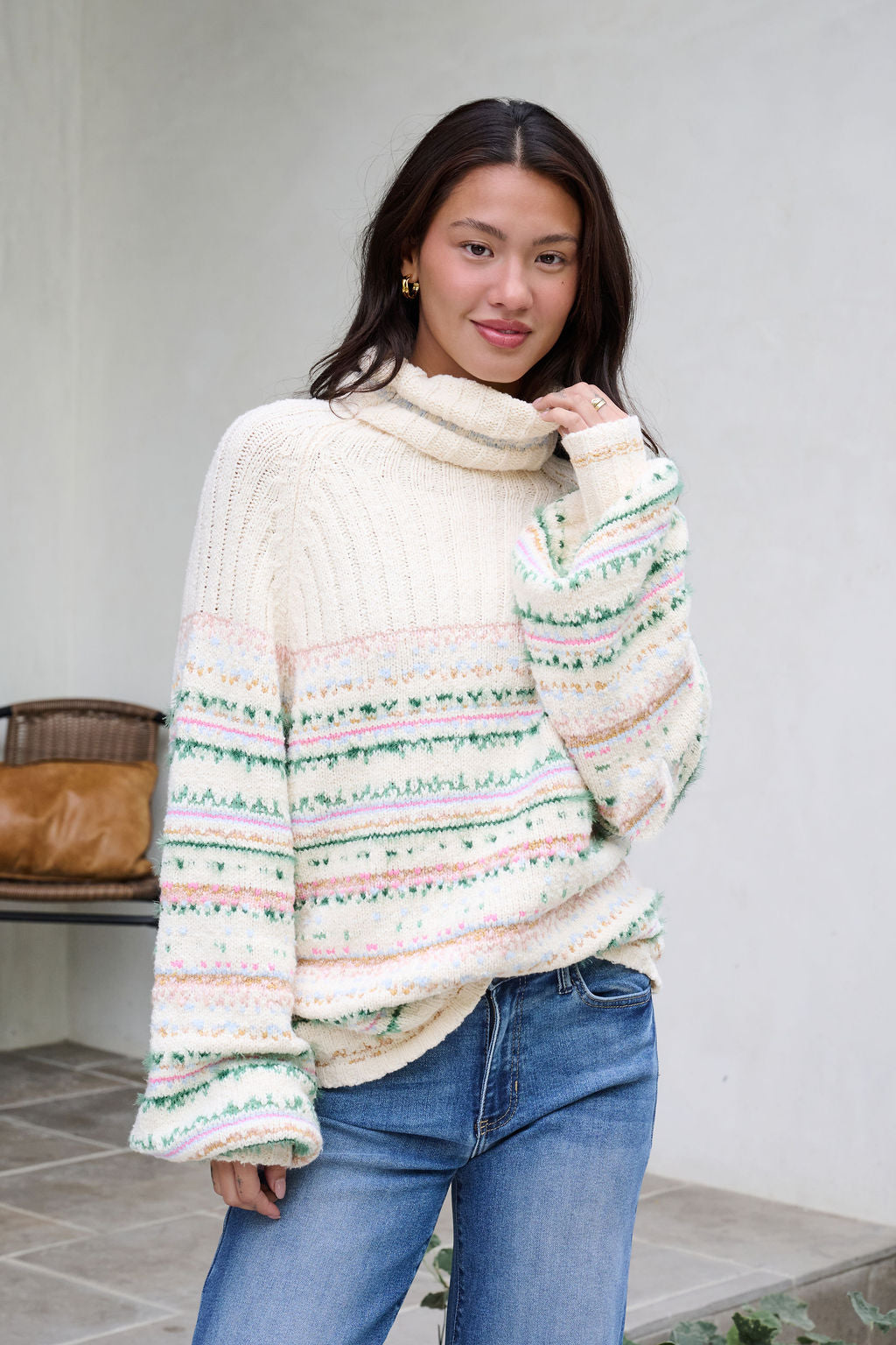 A woman models the Cozy Cream Turtleneck Striped Sweater with jeans, smiling softly outdoors with holiday charm.