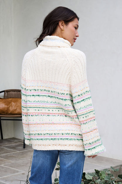 Woman with long dark hair wears the Cozy Cream Turtleneck Striped Sweater and blue jeans outdoors, facing away for holiday charm.