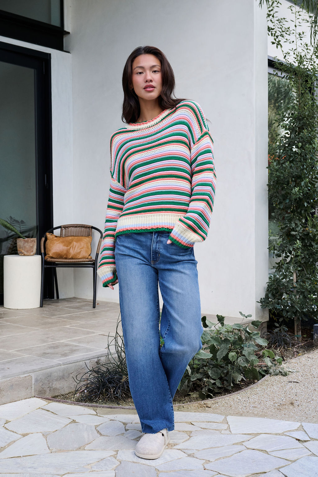 A woman wears an Ivory Multi Striped Crewneck Sweater and blue jeans outdoors—perfect for your winter wardrobe.
