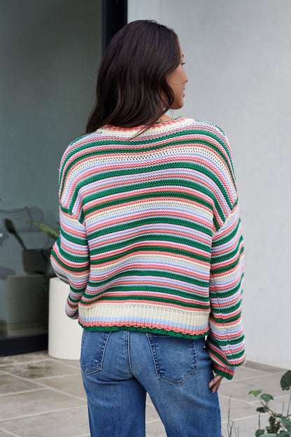 A woman with long dark hair, seen from behind, wears an Ivory Multi Striped Crewneck Sweater and blue jeans outdoors.