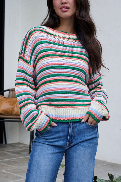 Woman wears an Ivory Multi Striped Crewneck Sweater and blue jeans outdoors, hands in pockets near a chair and bag.