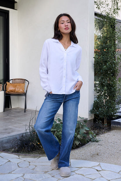 Woman wears the Thread and Supply White Button Down Presley Top with blue jeans outdoors, one hand in her pocket.