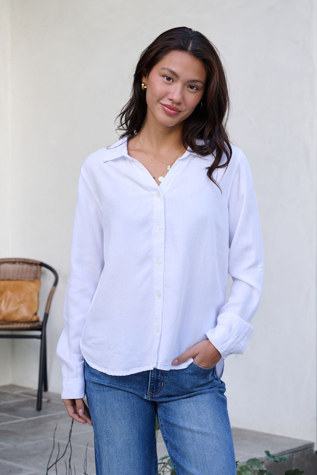 Woman with long dark hair wears a Thread and Supply Presley Top in white, paired with blue jeans, smiling outdoors at the camera.