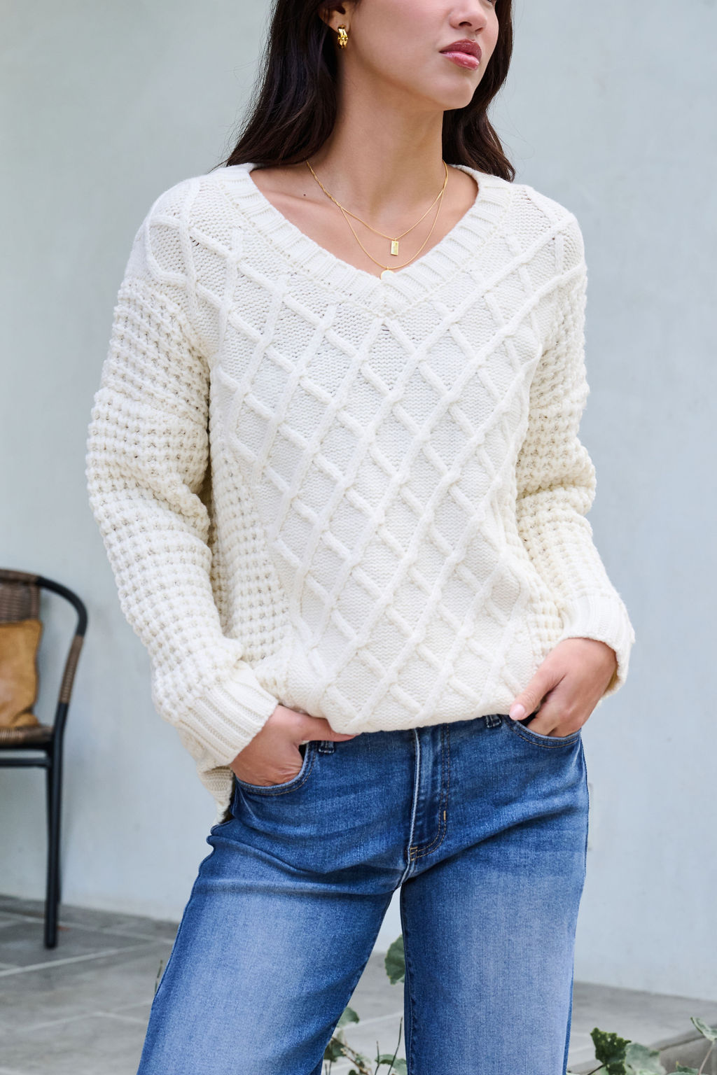 Woman models the Ivory Textured Cable Knit Sweater with blue jeans, standing hands in pockets against a minimal neutral backdrop.