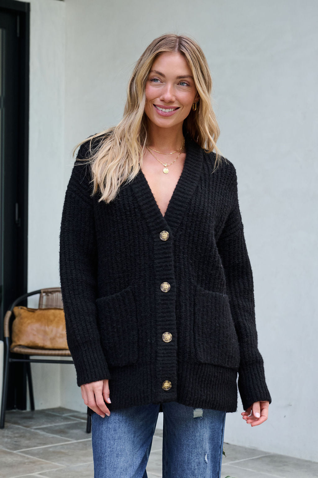 Woman smiling in a Black Heavy Knit Button Down Cardigan and blue jeans—an ideal pick for your winter wardrobe.