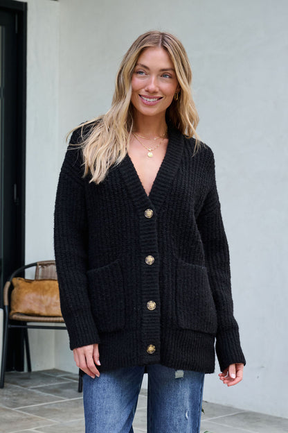 Woman smiling in a Black Heavy Knit Button Down Cardigan and blue jeans—an ideal pick for your winter wardrobe.