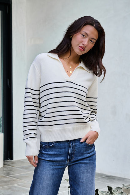 Woman in an Ivory and Black Stripe Ribbed Sweater with blue jeans—ideal for updating your winter wardrobe.