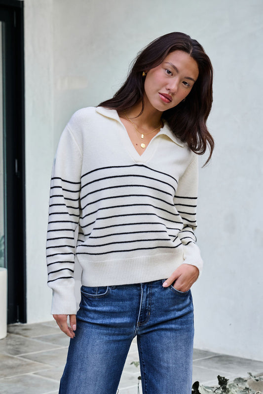 Woman in an Ivory and Black Stripe Ribbed Sweater with blue jeans—ideal for updating your winter wardrobe.
