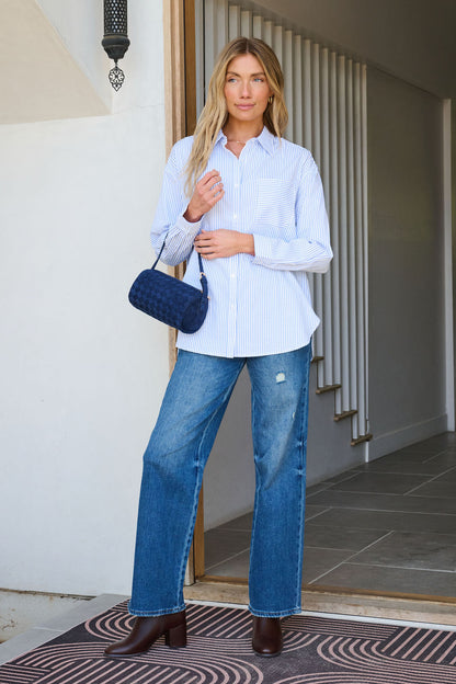 Woman stands in a doorway wearing the Blue and White Striped Open Back Tie Top, blue jeans, brown boots, holding a blue purse.