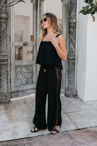 Woman in ELAN Black Lace Trim Wide Leg Pants, sunglasses, and sandals stands by ornate wooden doors outdoors.