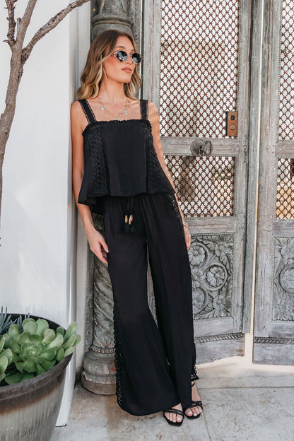 Woman in sunglasses wears ELAN Black Lace Trim Wide Leg Pants, standing by ornate doors next to a large potted plant.