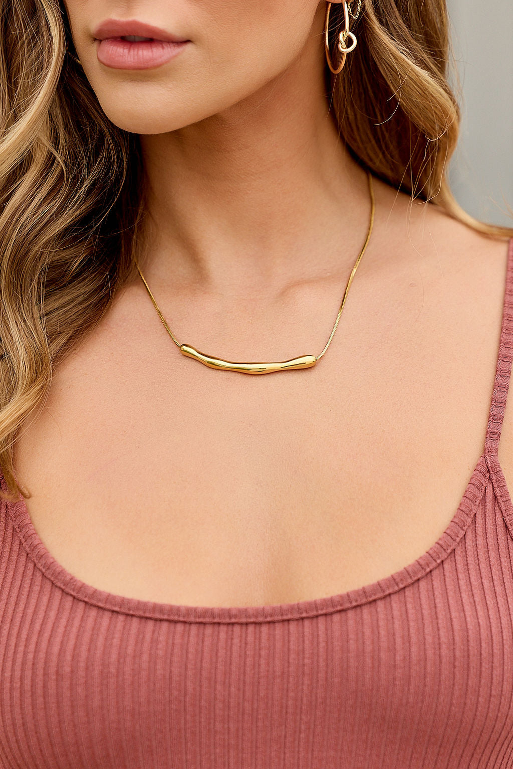 Woman wears a ribbed mauve tank, gold earrings, and the Golden Bar Pendant Necklace; only her neck and lower face are visible.