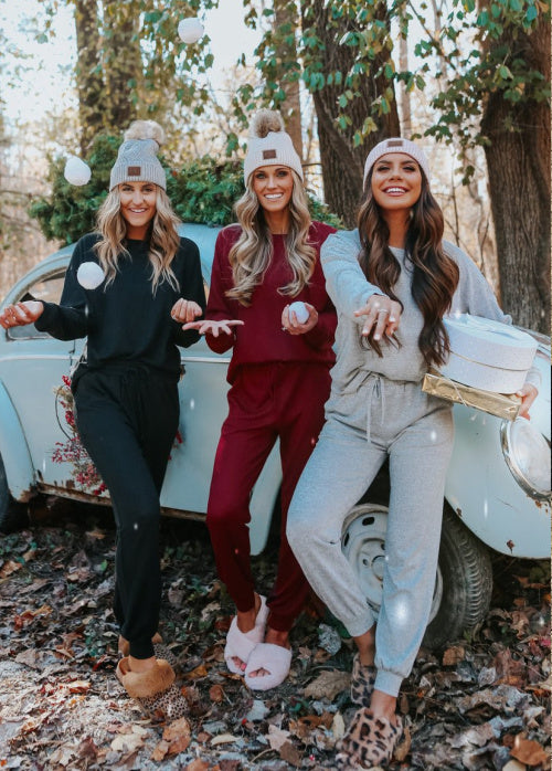 Three women in matching outfits standing in front of a vintage car in a forest setting.