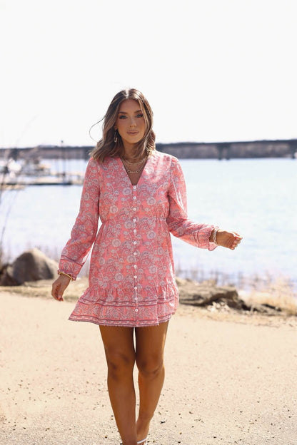 Woman in a Rosie Pink Floral Print Buttoned Mini Dress - DOORBUSTER, walking outdoors by water with boats in the background.
