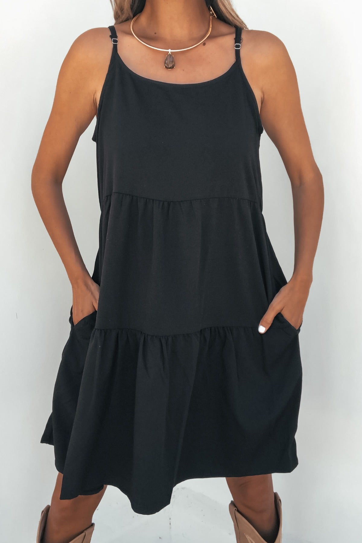 Model wearing the On Point Tiered Mini Dress - Black with adjustable straps and pockets, standing against a white background.
