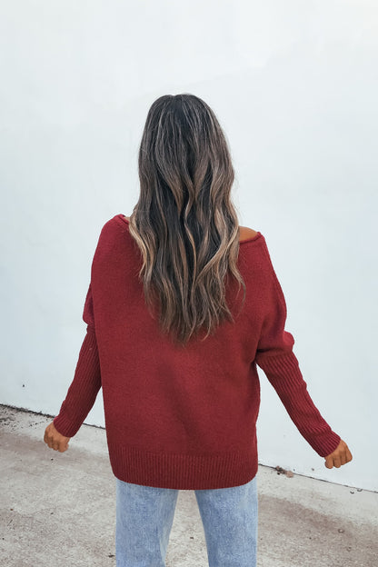Woman with wavy brown hair wearing the Off The Shoulder Ribbed Sweater - Wine and light jeans, back facing the camera.