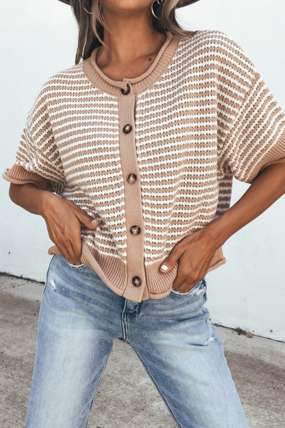 Woman in a tan striped button down sweater and light blue jeans, standing outdoors.
