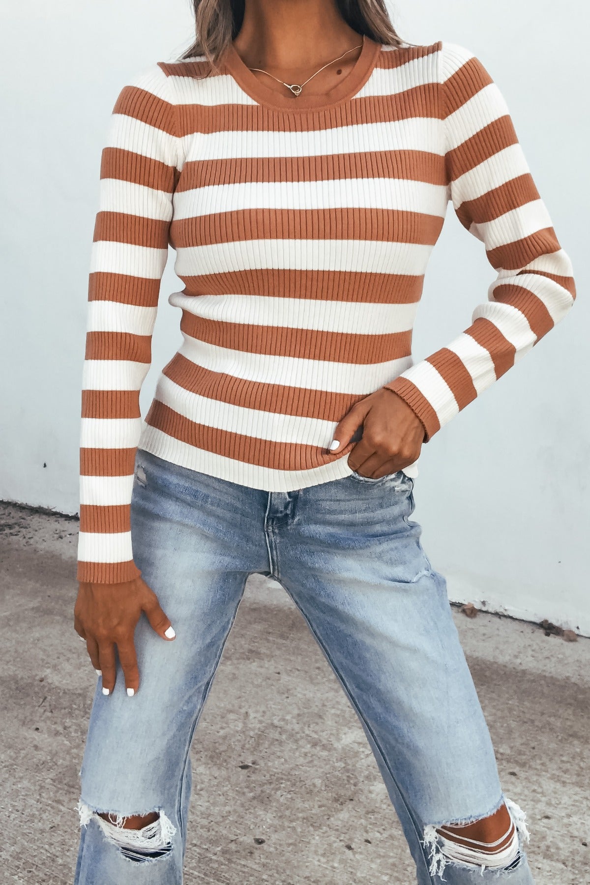 Woman wears Ivory Striped Long Sleeve Top with ripped light blue jeans, highlighting a fitted look outdoors.