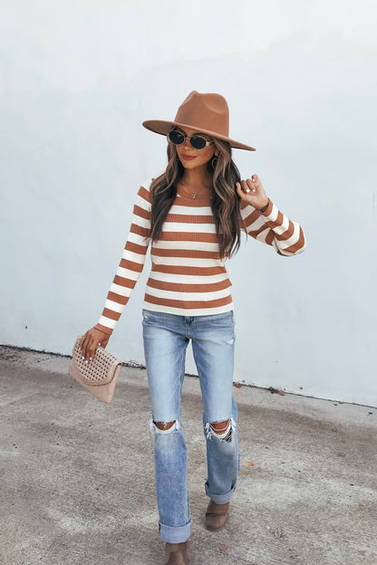Woman in an Ivory Striped Long Sleeve Top, sunglasses, ripped jeans, and boots holds a clutch against a light plain background.
