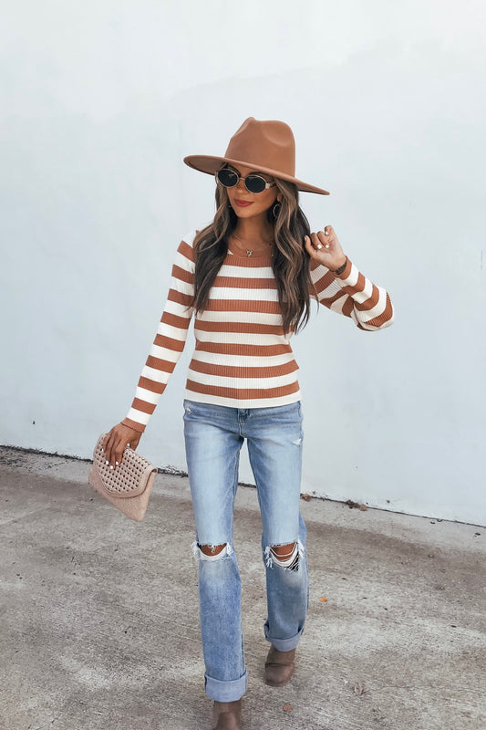 Woman in an Ivory Striped Long Sleeve Top, sunglasses, ripped jeans, and boots holds a clutch against a light plain background.