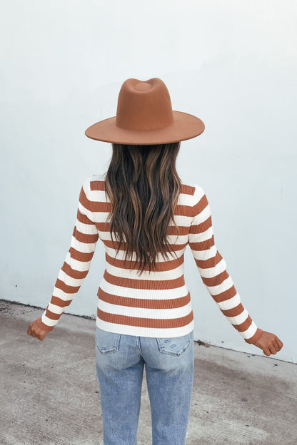 Someone in an Ivory Striped Long Sleeve Top and blue jeans stands facing a light wall, arms out, wearing a brown hat.