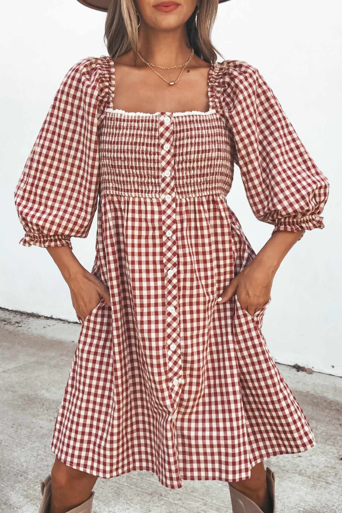 Woman in a Gingham Babydoll Mini Dress - Burgundy, featuring puff sleeves, mini length, and pockets, standing outdoors.