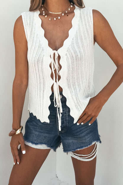 Woman wears a cream Sunlace Tie Front Sweater Vest, distressed denim shorts, layered necklaces, and a bracelet against a white background.