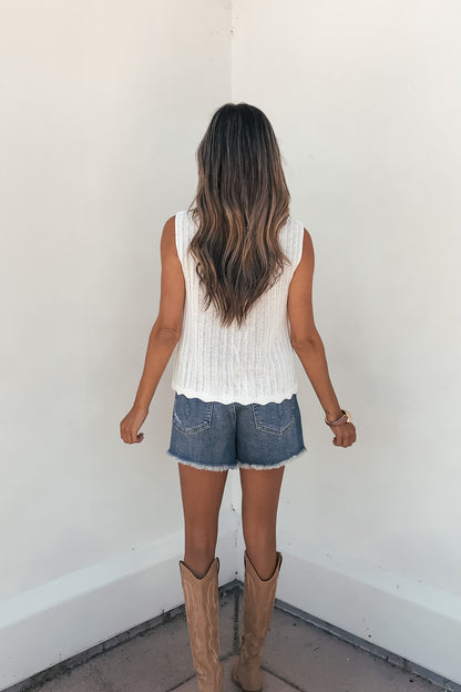 Woman with long wavy hair wears the Sunlace Tie Front Sweater Vest in cream, facing a white wall.