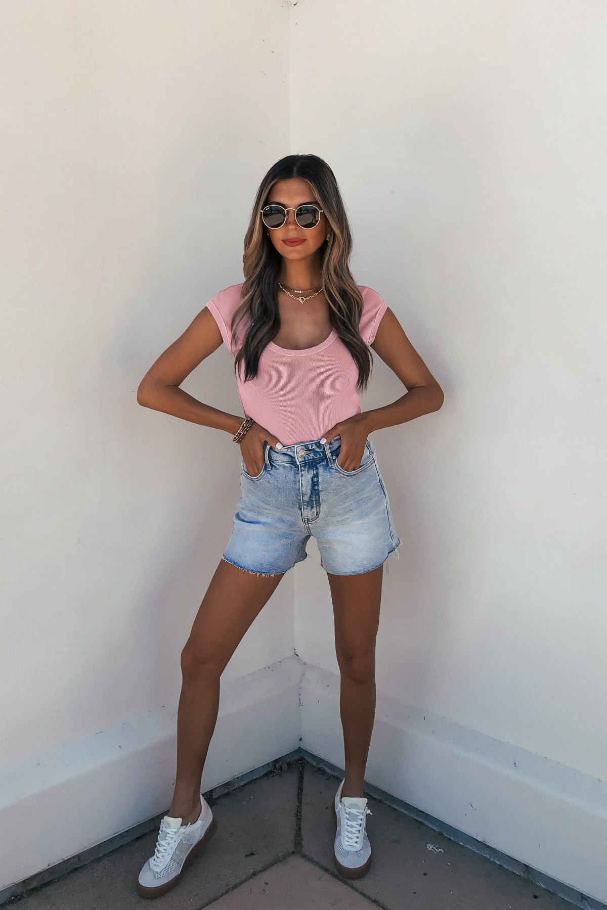 Woman in Dusty Mauve Scoop Neck Ribbed Top and denim shorts stands by white wall; casual summer outfit.