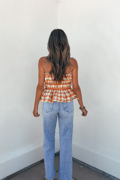 A woman with long wavy hair wears the Aureum Multi Plaid Smock Top and light blue jeans, facing a white wall with her back to camera.