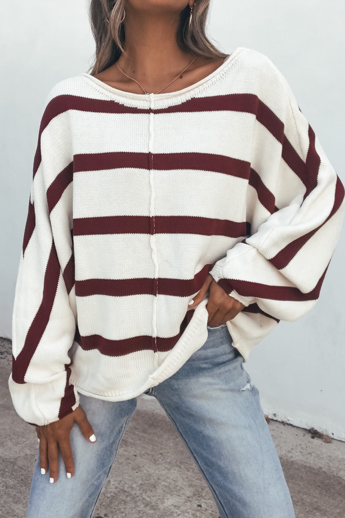 Woman in a Burgundy Striped Dolman Sleeve Sweater and light blue jeans, standing outdoors.