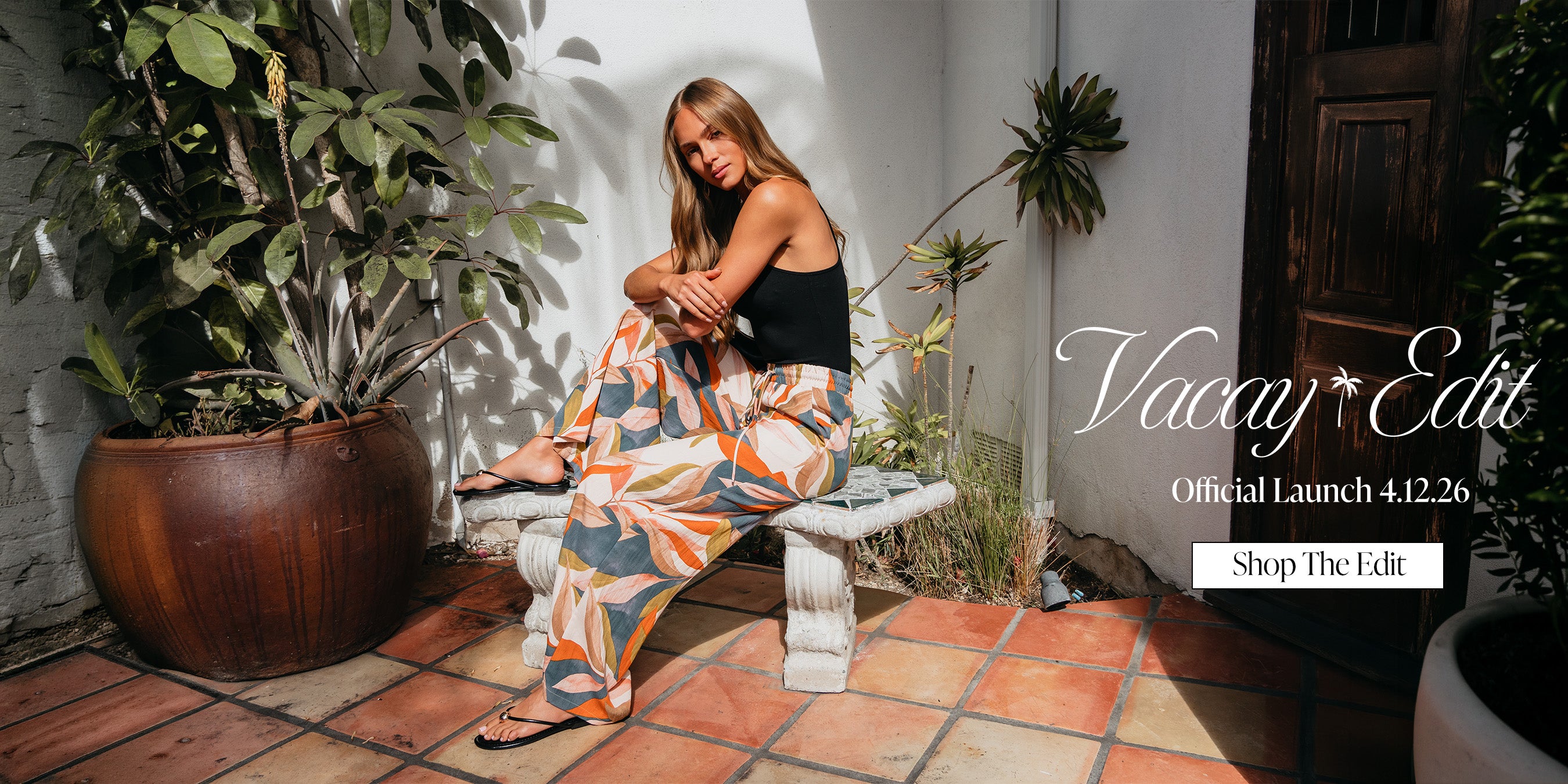 Woman in a colorful dress sitting on a stone bench with plants around her, promoting 'Vacay Edit' with a launch date.