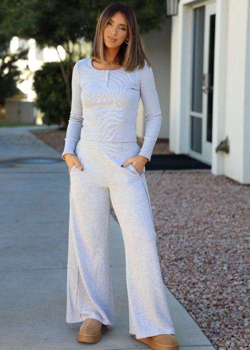 Woman wearing a light blue long-sleeve top and white wide-leg pants standing on a sidewalk.